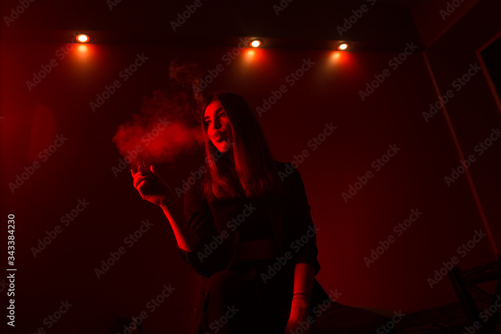 Girl model smokes vape in red light. Girl model smokes vape in red light.