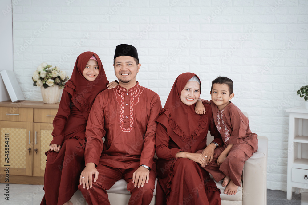 Asian family wearing Malay traditional clothes sitting on the sofa with the concept of Eid Mubarak