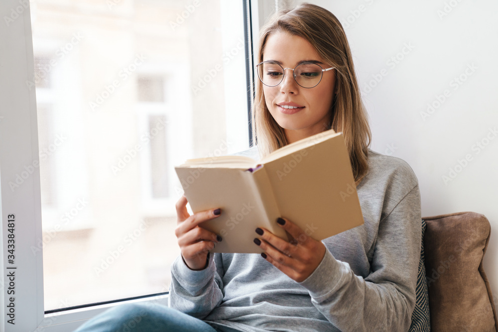 Photo of serious woman reading book while sitting near window Photo of serious woman reading book while sitting near window