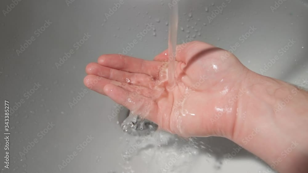 a stream of pure transparent water flows in the palm of the hand against a white ceramic sink. slow motion a stream of pure transparent water flows in the palm of the hand against a white ceramic sink. slow motion