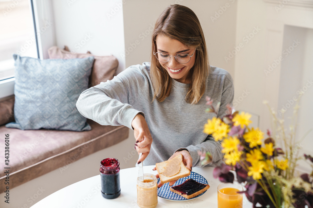 Photo of cheerful young woman eating toasts while having breakfast