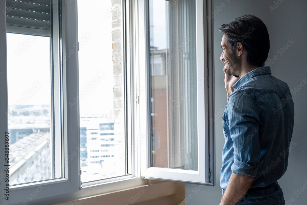 Handsome single man staying near window in his house and talking on phone Handsome single man staying near window in his house and talking on phone
