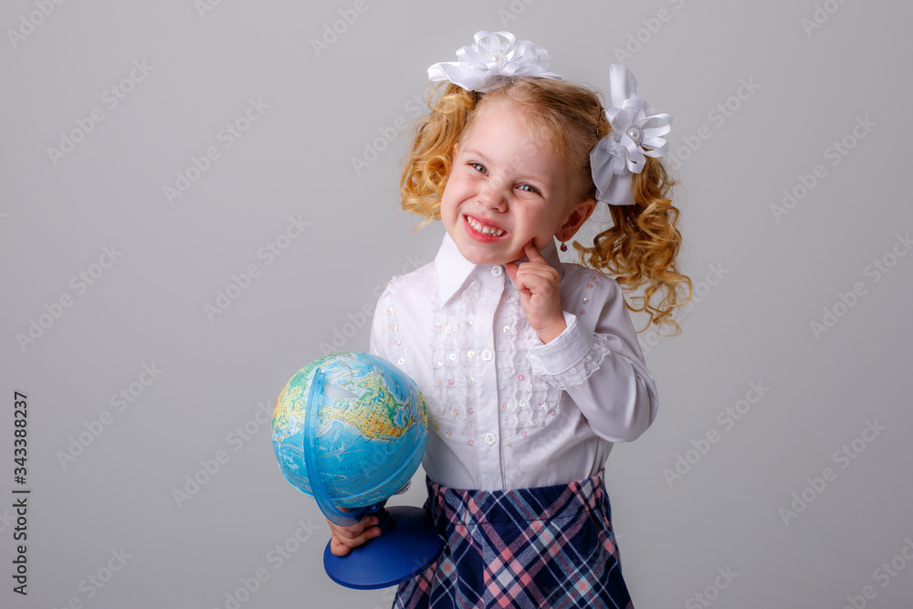 a small curly haired blonde girl in a school uniform holds a globe in her hands thinking on a white background a small curly haired blonde girl in a school uniform holds a globe in her hands thinking on a white background