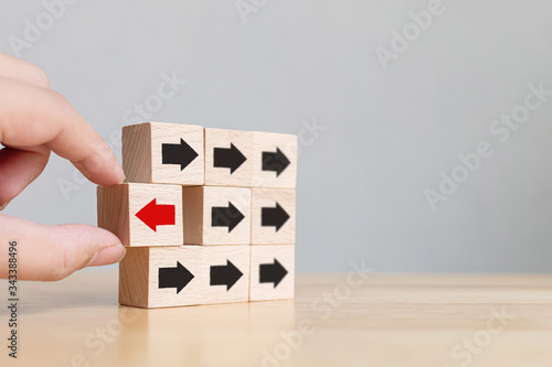 Hand choosen wooden block with red arrow facing the opposite direction black arrows, Unique, think different, individual and standing out from the crowd concept. photo