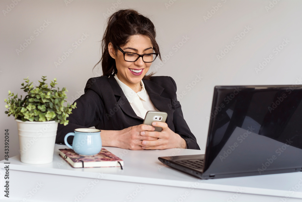 Beautiful Young Woman in front of the Laptop ,Working from Home with Smartphone in the Hands Beautiful Young Woman in front of the Laptop ,Working from Home with Smartphone in the Hands