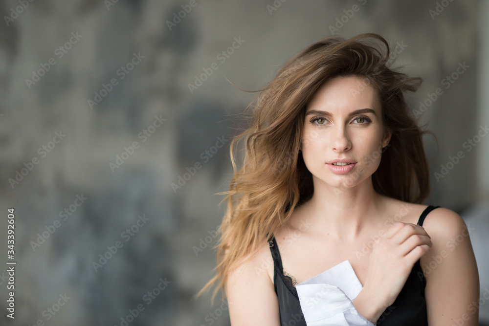 Beautiful elegant woman with flying hair and full lips in a white shirt on a gray background looks languidly at the camera. Beauty and fashionable style. Soft selective focus.