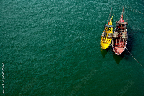 A view from above on two boats, red and yellow which are located on the blue water, the river.