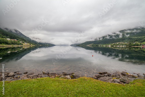 Norwegian fjord and mountains surrounded by clouds, ideal fjord reflection in clear water. selective focus.