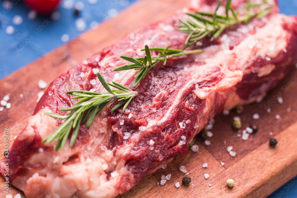 Raw meat. A large piece of beef chop on a wooden cutting board with rosemary and spices, close-up.