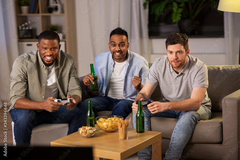 friendship, technology and leisure concept - smiling male friends with gamepads and beer playing video game at home at night friendship, technology and leisure concept - smiling male friends with gamepads and beer playing video game at home at night