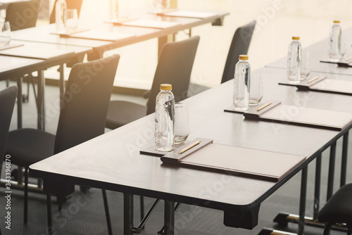 Plastic water bottles, Drinking glasses with pencil and white papers setup on the table prepared for seminar or business meeting in the hotel conference room