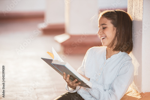 Smiling girl reading a book sitting on the rooftop