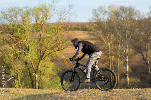 Sports brutal bearded guy on a modern mountain bike. Cyclist on the green hills in the spring.