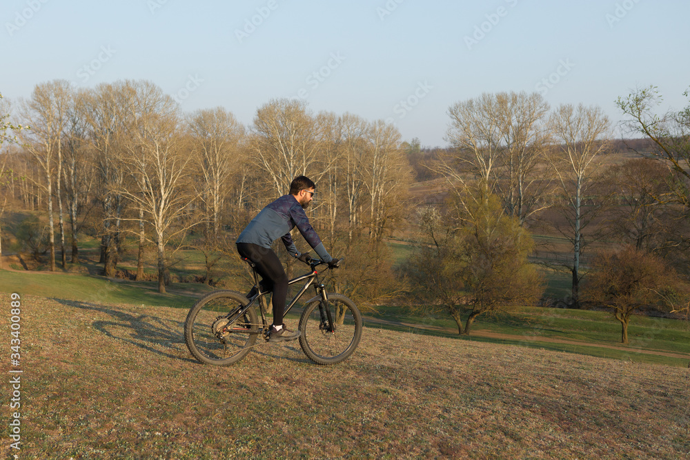 Cyclist in shorts and jersey on a modern carbon hardtail bike with an air suspension fork standing on a cliff against the background of fresh green spring forest