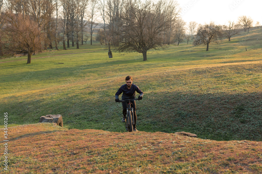 Fototapeta premium Cyclist in shorts and jersey on a modern carbon hardtail bike with an air suspension fork standing on a cliff against the background of fresh green spring forest
