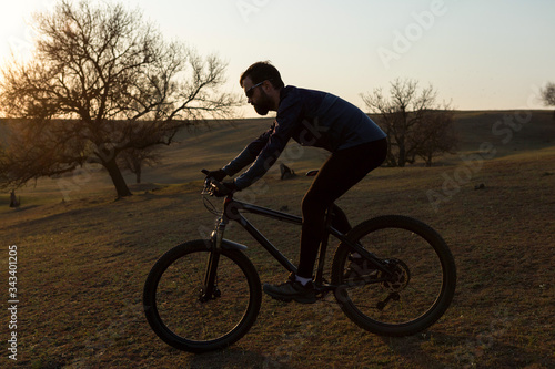 Cyclist in shorts and jersey on a modern carbon hardtail bike with an air suspension fork standing on a cliff against the background of fresh green spring forest