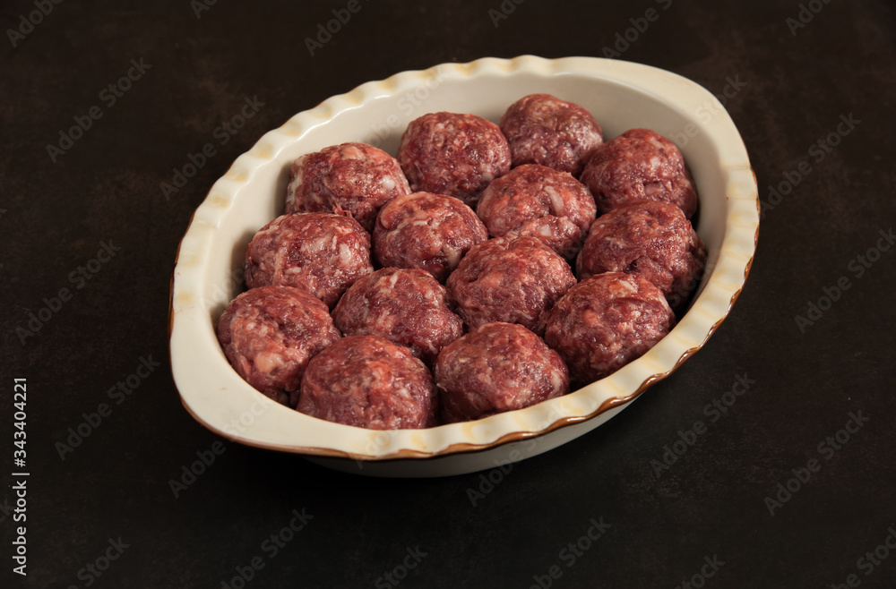 Juicy homemade beef patties in a ceramic baking dish are close-up ready for cooking on a dark background in the kitchen. Selective focus. Juicy homemade beef patties in a ceramic baking dish are close-up ready for cooking on a dark background in the kitchen. Selective focus.