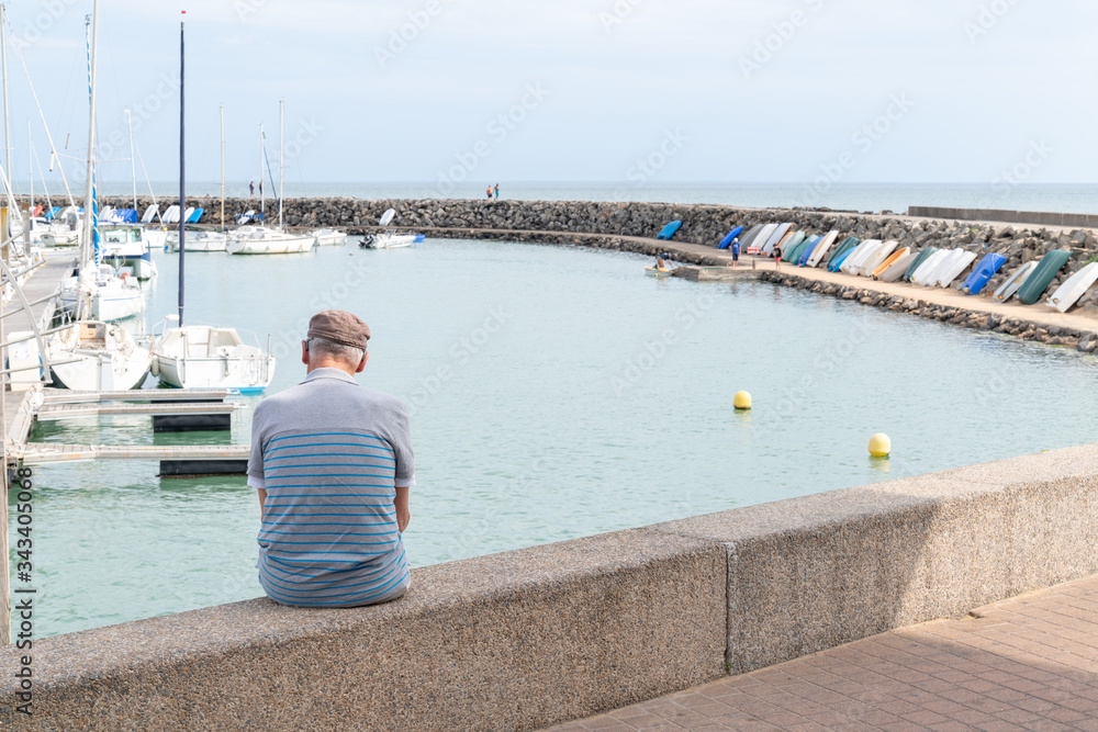 senior retired elderly man sitting on a bench looking ocean atlantic harbor Jard sur mer port in vendée