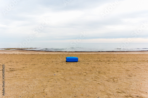 A red travel suitcase is alone on a beach with the sea or ocean in the background. Voyage, tropical beach vacation in the sun.
