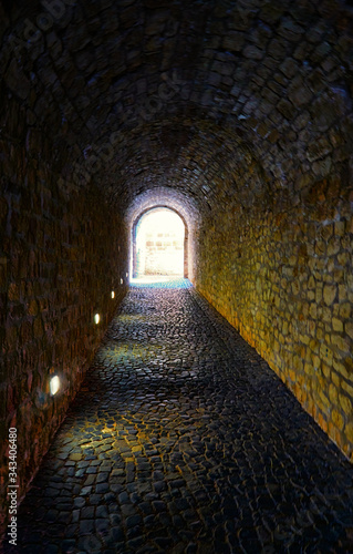 Dark tunnel made of natural stones with light at the end.