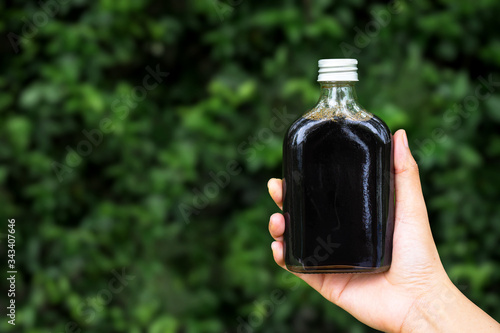 women hand holding cold brew coffee bottle on green nature blurred background