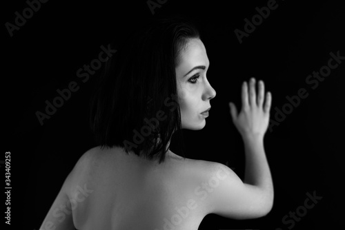 Back view black and white portrait of young beautiful woman holding background and looking aside.