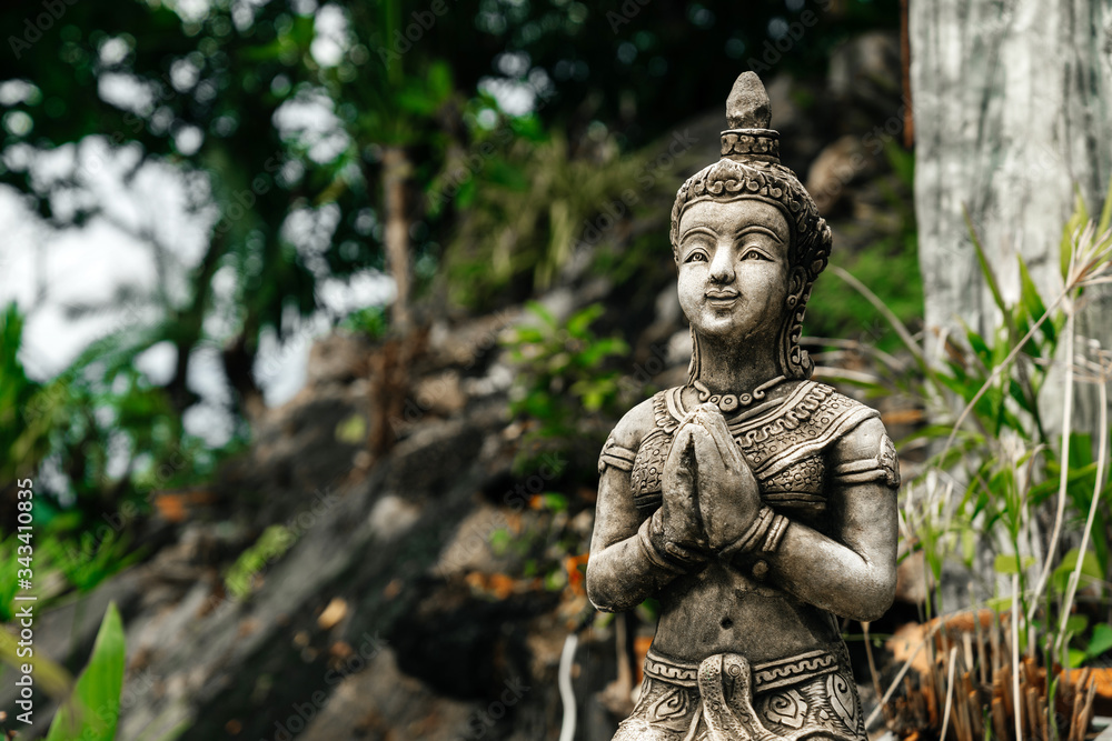 Stone statue of a man with hands in prayer in tropical greenery and the Asian jungle.