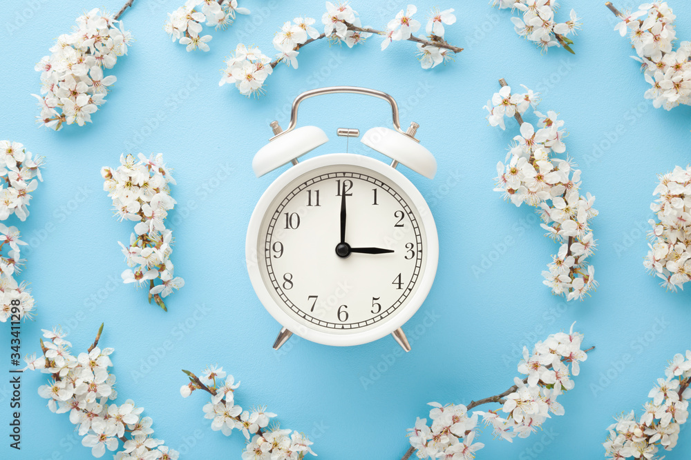 Alarm clock with branches of white cherry blossoms on light blue table ...