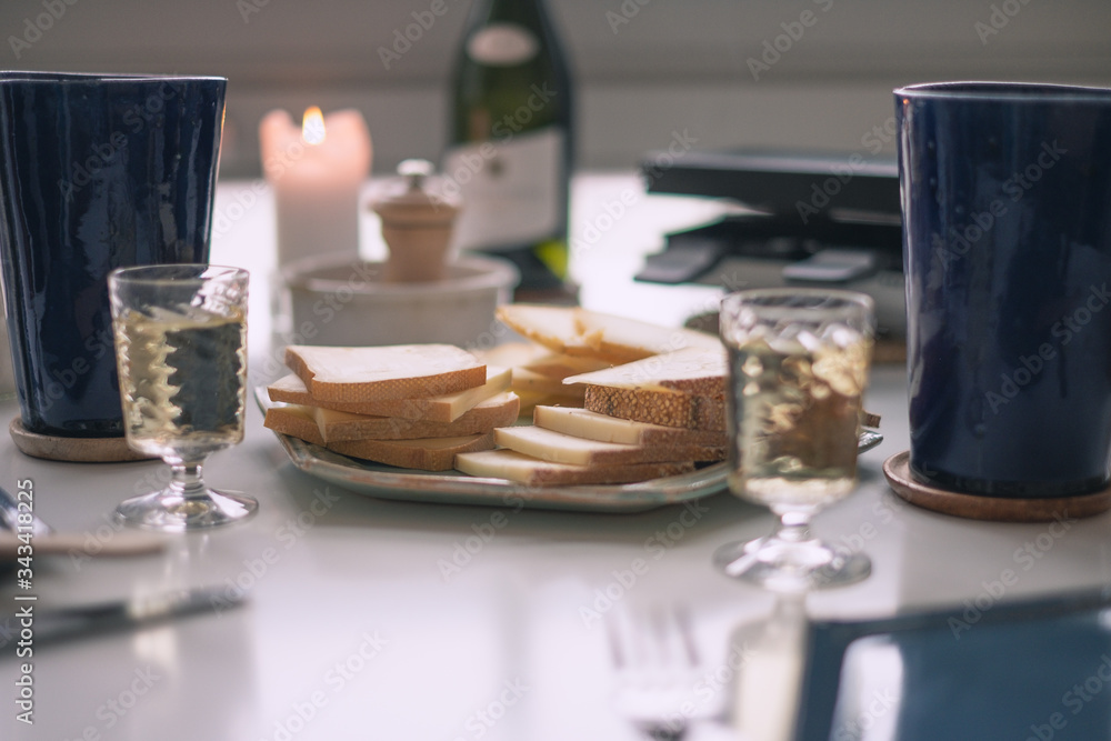 Dinner table, with slices of raclette cheese, a raclette machine, two glasses and a bottle of white wine, candle, ceramic mugs and pepper, ready for a nice traditional and typical swiss dinner.