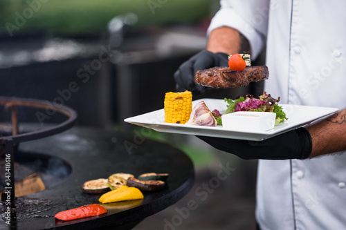 Man putting beef steak on a white plate with grilled vegetables