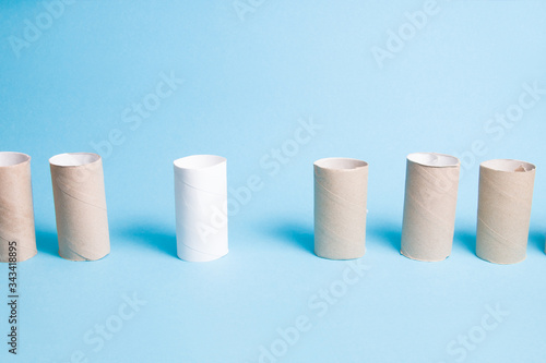 hubs from toilet paper stand in a row, social distance concept, blue background, copy space, one sleeve is white and stands at a distance