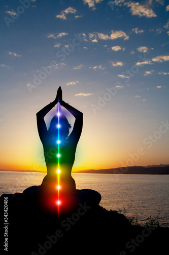 Silhouette of woman sits in a lotus pose on beach sunset view  glowing seven all chakra. Kundalini energy. girl practicing yoga meditation outdoors
