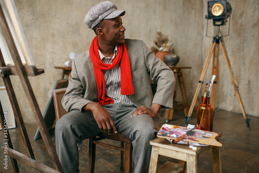 Painter in hat and red scarf poses at easel
