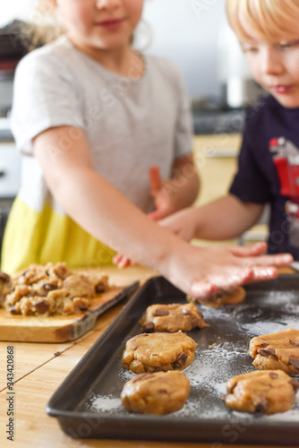 Kids making cookies in kitchen placing dough on tray for cooking at home