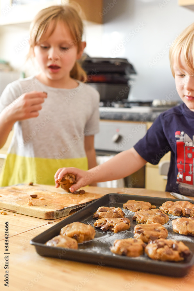 Kids making cookies in kitchen placing dough on tray for cooking at home