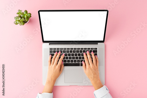 Overhead shot of office desktop with female hands working on laptop with copyspace. Business background with small flower. Flat lay