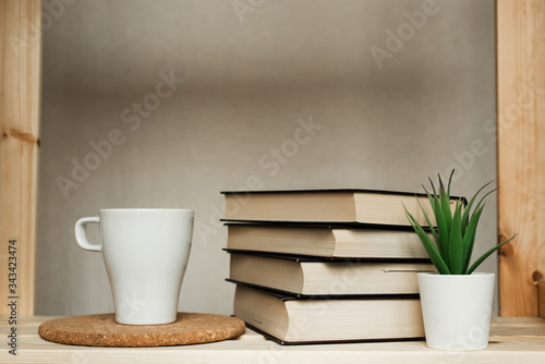 A stack of books on the shelf. Books and a mug of tea on the shelf.