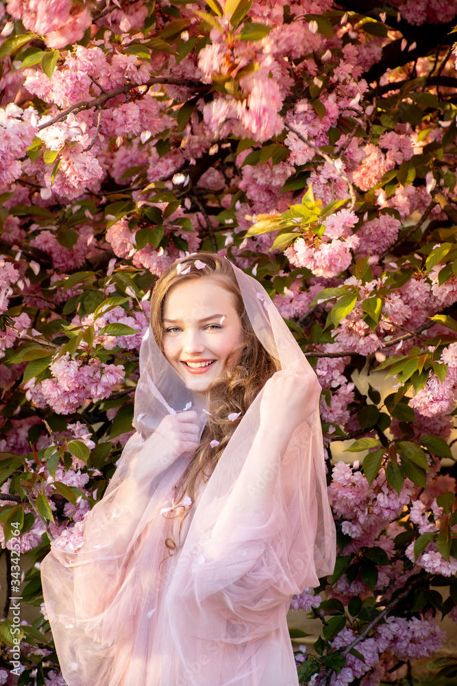 portrait of a beautiful teenager girl in delicate sakura flowers with a veil