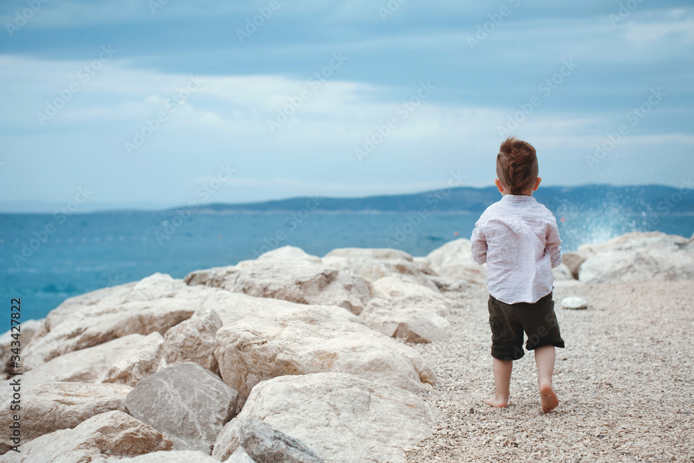 Baby boy stands with his back on the seashore.