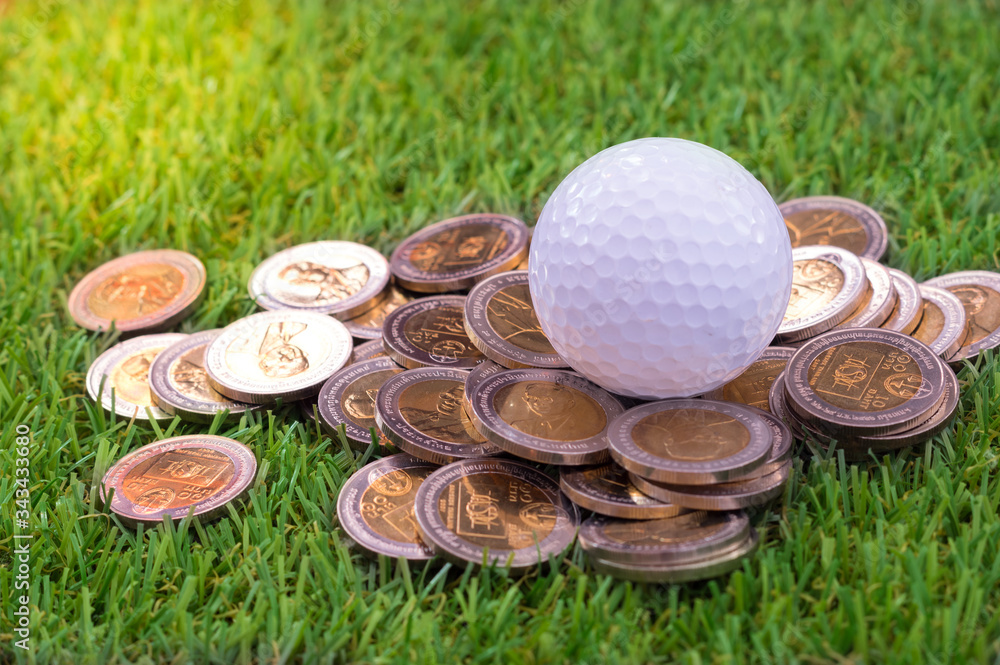 Naklejka premium Golf ball with golden coins on green grass.