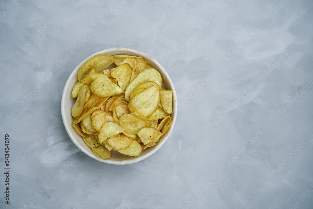 Sweet Banana chips. Heap of dried banana sliced snack with sweet taste in white bowl with grey background. (isolated, top view) Sweet Banana chips. Heap of dried banana sliced snack with sweet taste in white bowl with grey background. (isolated, top view)