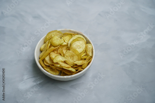 Sweet Banana chips. Heap of dried banana sliced snack with sweet taste in white bowl with grey background. (isolated)