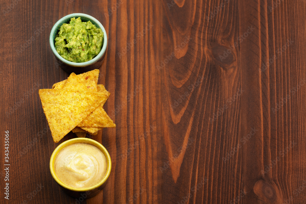 Tortilla chips nachos, sauce guacamole and cheese sauce on wooden background. Space for text Tortilla chips nachos, sauce guacamole and cheese sauce on wooden background. Space for text