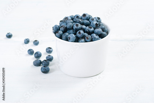 bilberry fruits at white ceramic cup, on bright wood table photo