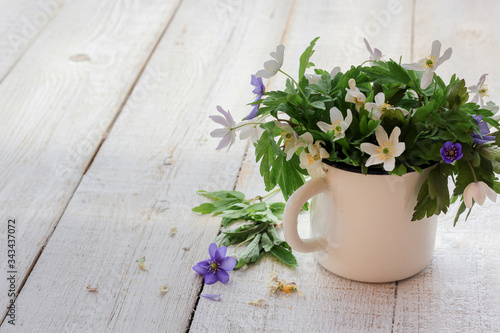 Wood anemones in a rustic cup on a white wooden table with a copy space