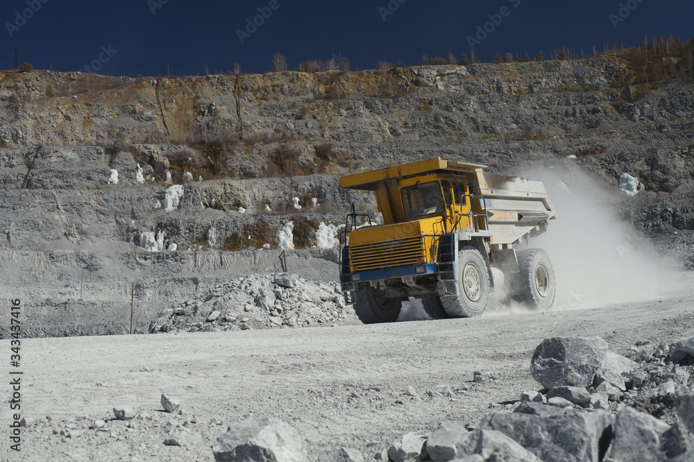 Heavy mining dump truck transports stone ore in a quarry for the extraction of limestone. Heavy mining equipment. Heavy mining dump truck transports stone ore in a quarry for the extraction of limestone. Heavy mining equipment.