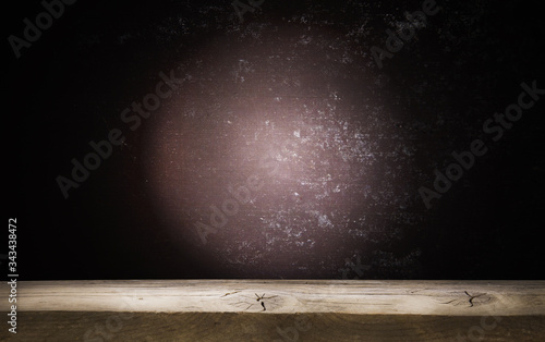Old wooden table top with a dirty concrete block wall in a dark room background.