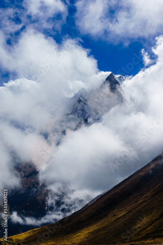 Peak of Machhapuchhre or fishtail mountain behind the clouds visible from Annapurna Base Camp during Annapurna Sanctuary trek in Nepal.