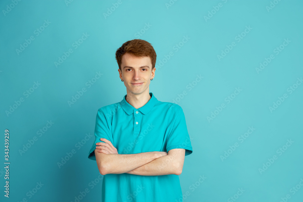 Hands crossed. Caucasian young man's modern portrait isolated on blue studio background, monochrome. Beautiful male model. Concept of human emotions, facial expression, sales, ad, trendy. Hands crossed. Caucasian young man's modern portrait isolated on blue studio background, monochrome. Beautiful male model. Concept of human emotions, facial expression, sales, ad, trendy.