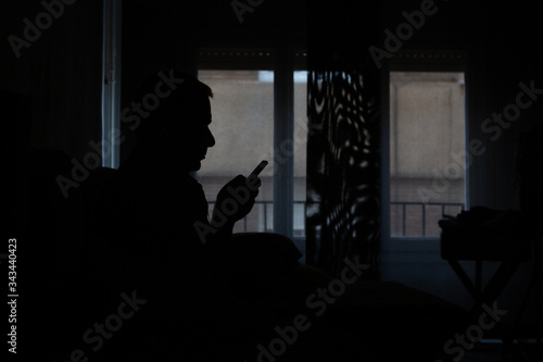 silhouette of a man looking at his cell phone at home